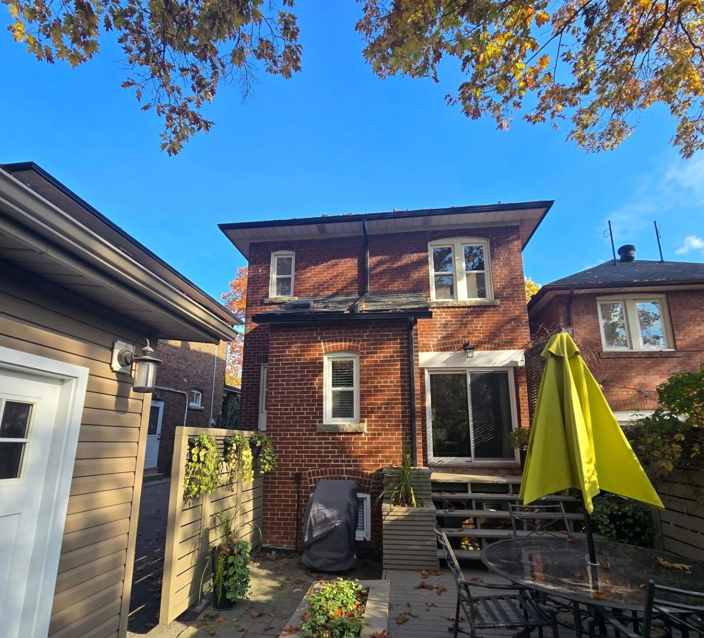 Backyard patio facing a brick two-story house with a green umbrella and patio furniture