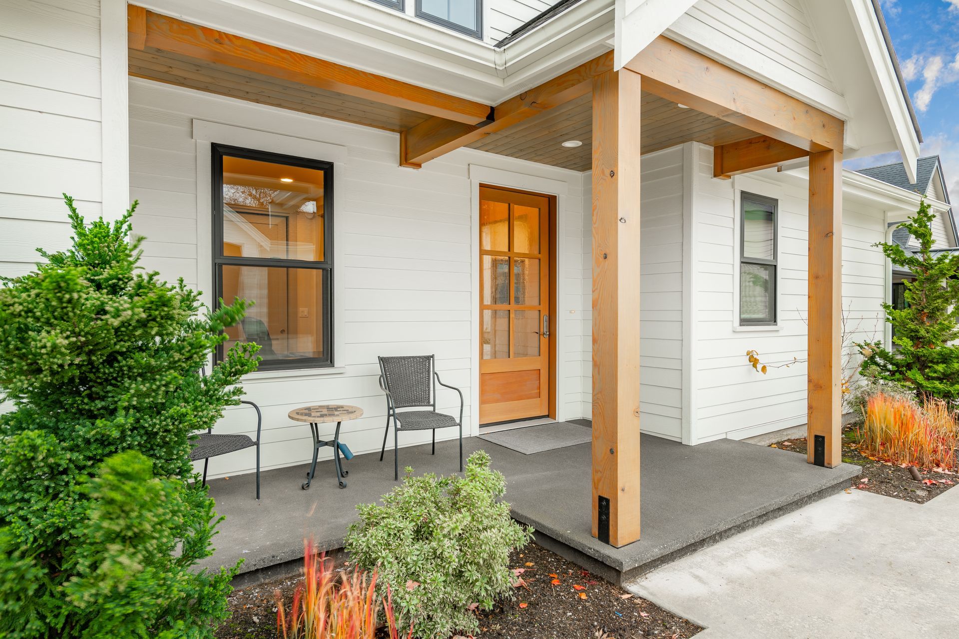 Front porch with wooden posts, two chairs, a small table, and a yellow front door at a modern home