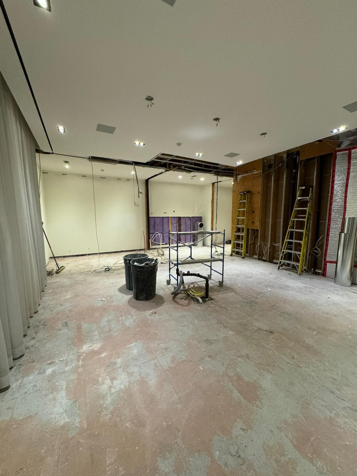 Interior of a room under construction, with exposed walls, ceiling, and debris on the floor.