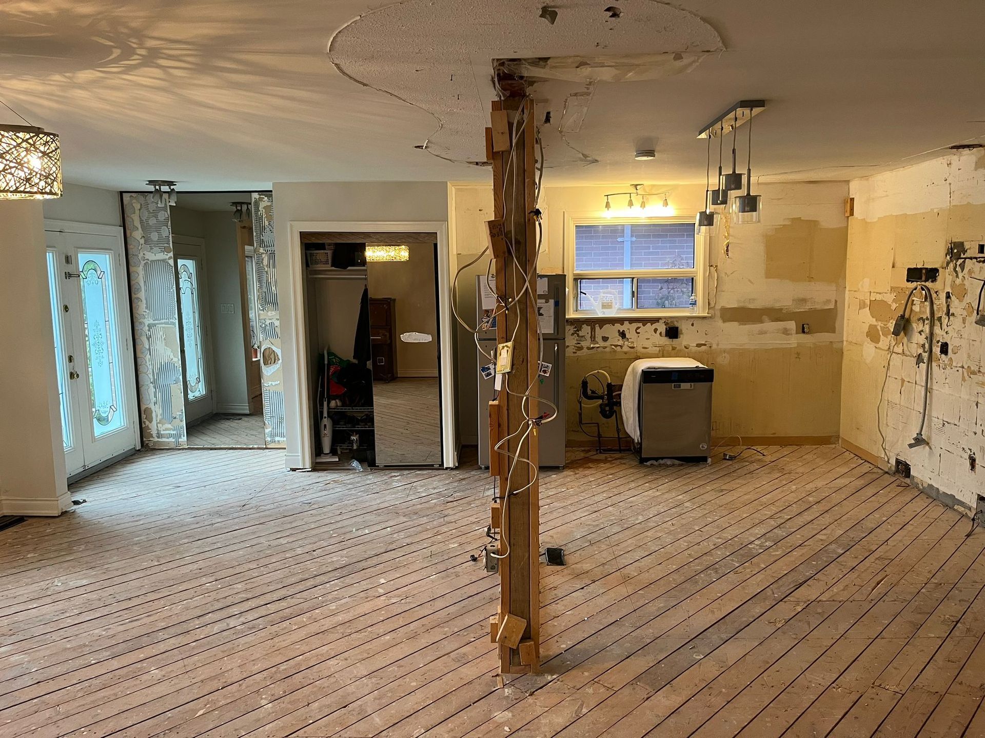 Interior of a room under renovation with exposed studs, ripped-out walls, and a central support beam.