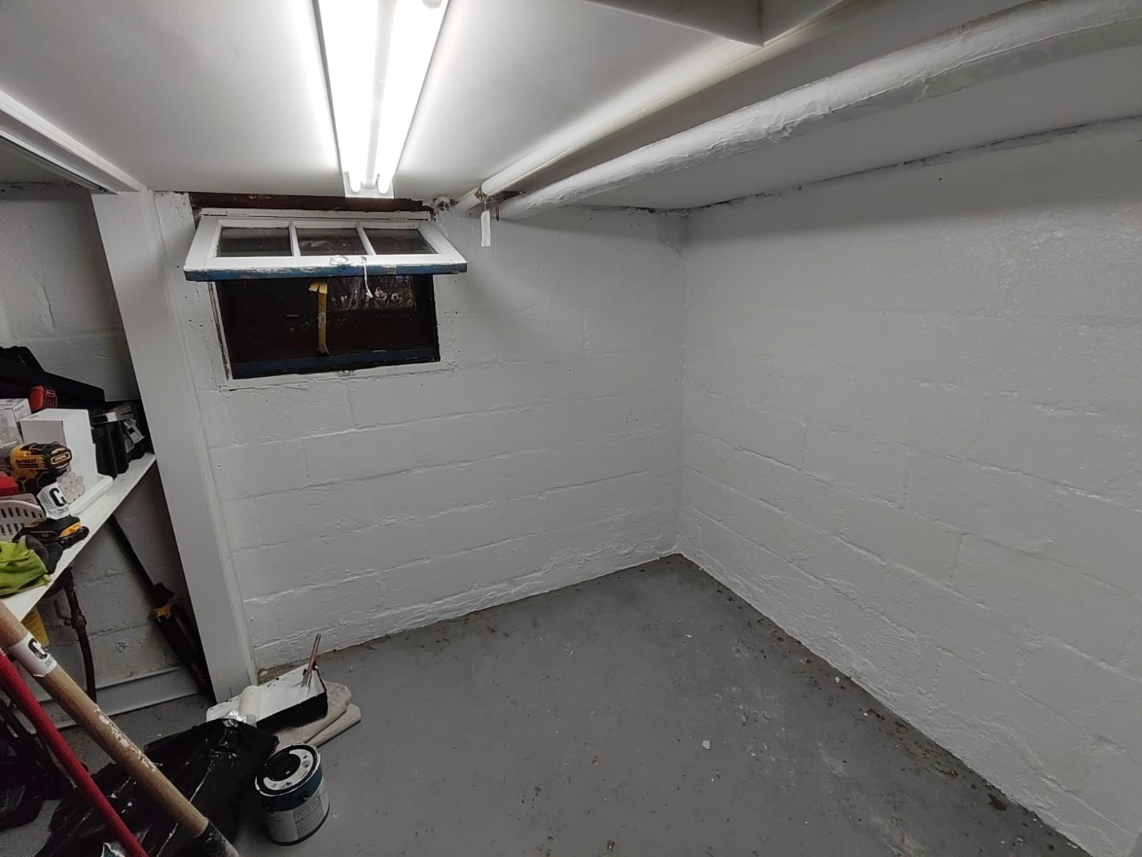 Small, painted white basement room with a gray floor, a window, and some tools.
