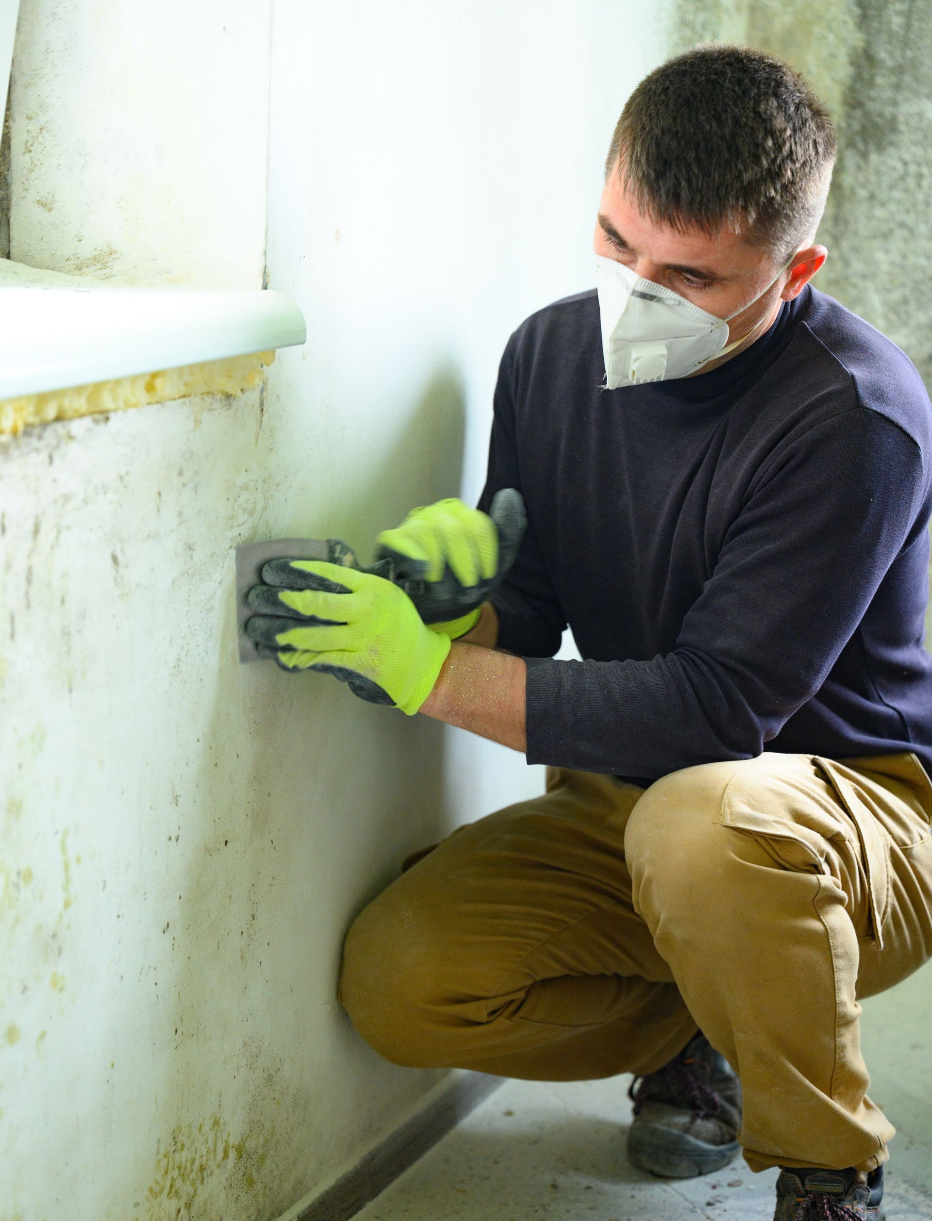 A man wearing a mask and gloves is cleaning a wall.