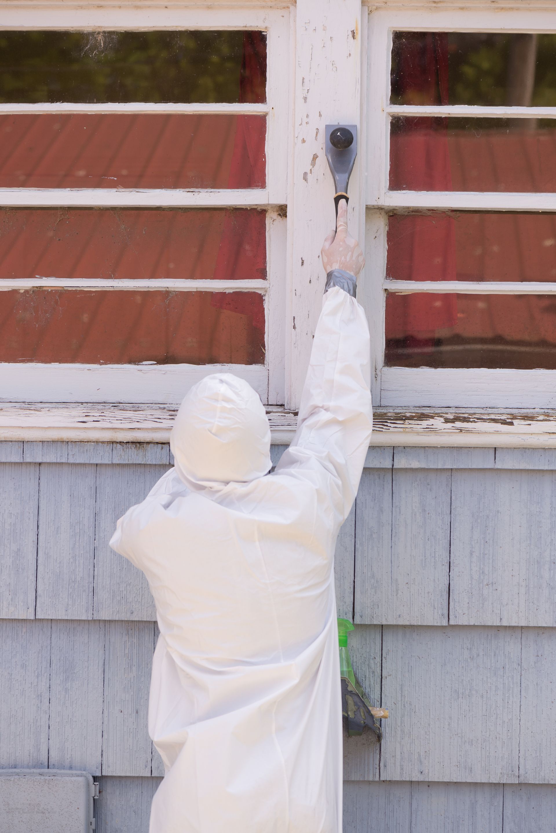 A person in a white coat is painting a window