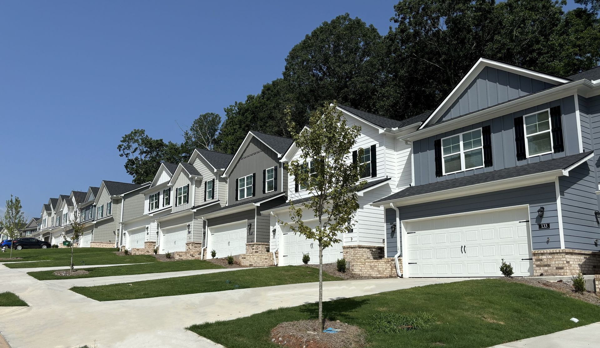 Row of modern suburban houses with garages and young trees along a quiet street