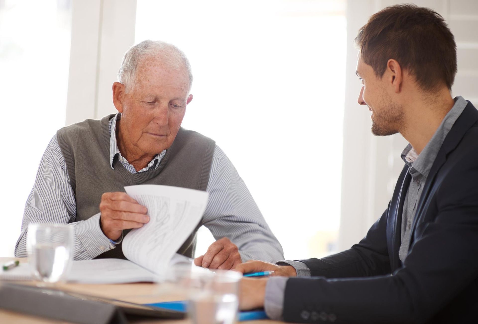 A professional in a suit reviews documents with an older individual wearing a sweater vest at a table.