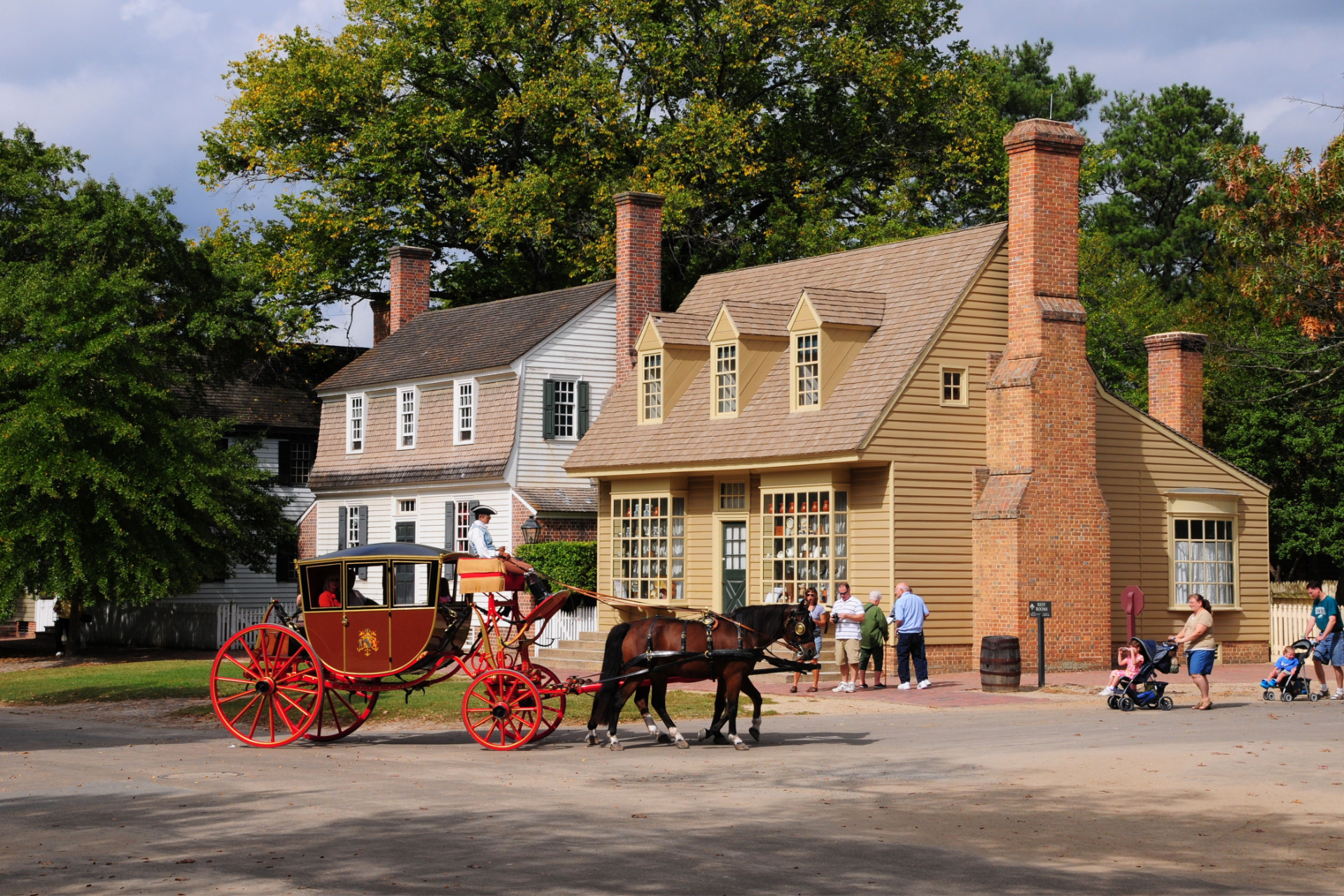 A red horse-drawn carriage sits in front of historic colonial-style buildings in Colonial Williamsburg.
