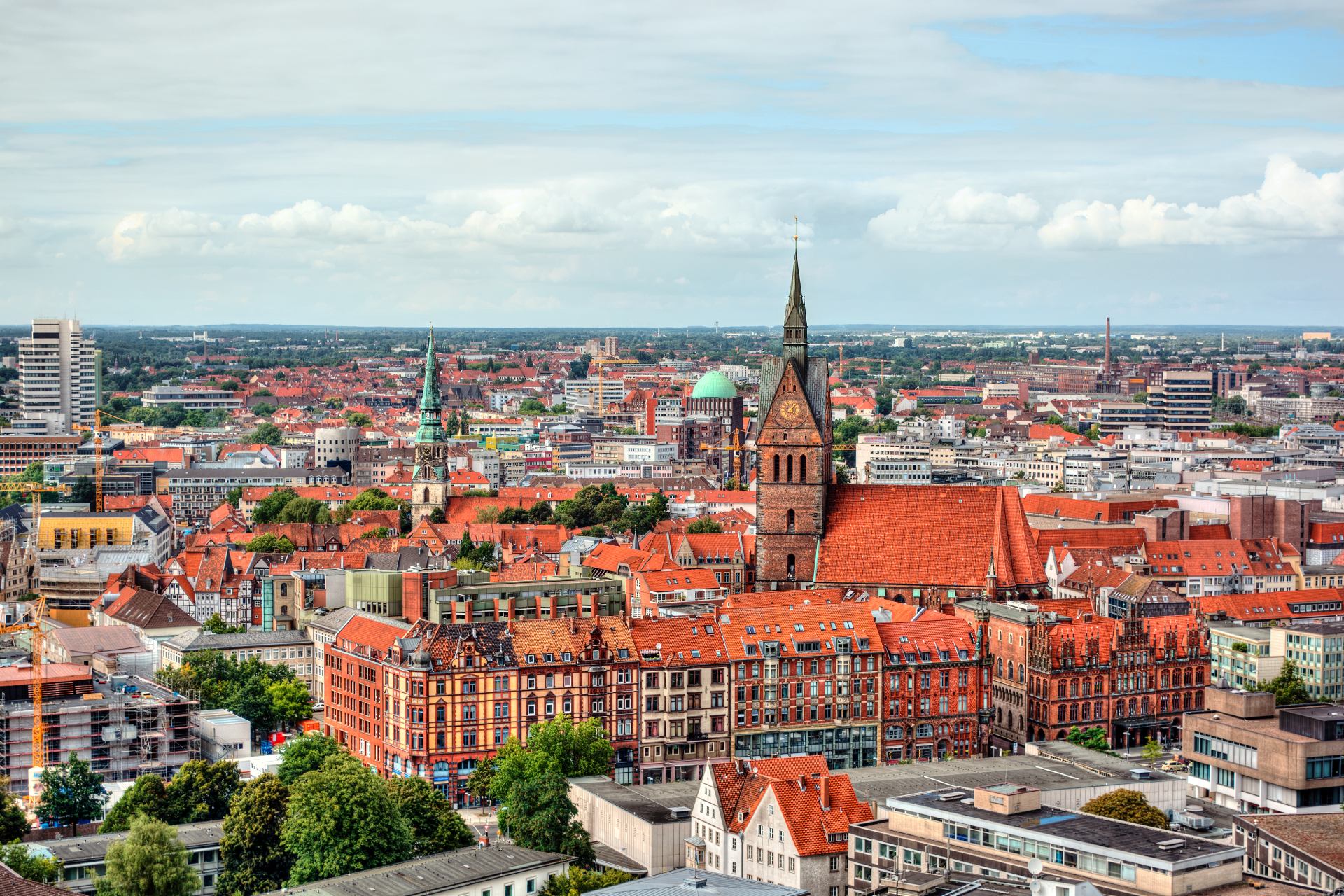 A high-angle view of the red-roofed cityscape of Hanover, Germany, featuring the prominent Marktkirche church spire.