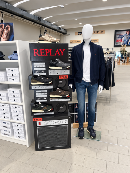 Abbigliamento maschile: camicia blu, gilet blu navy, giacca nera e pantaloni azzurri su un pavimento piastrellato.