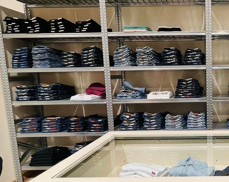 Scaffali pieni di jeans e camicie piegati in un negozio di abbigliamento, con colori diversi visibili.