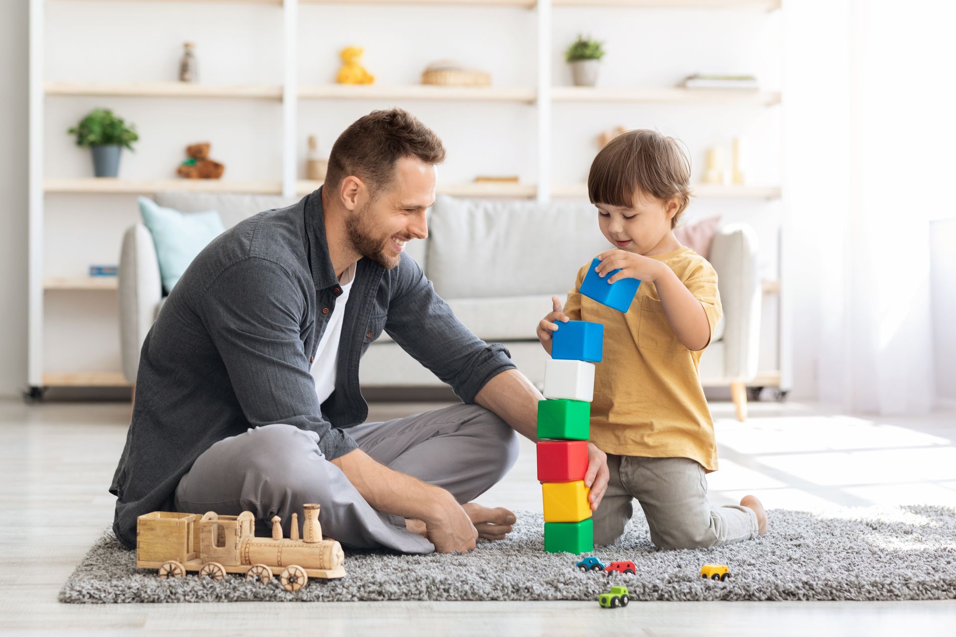 A person and a child sit on a rug playing with colorful toy blocks in a bright, modern living room.