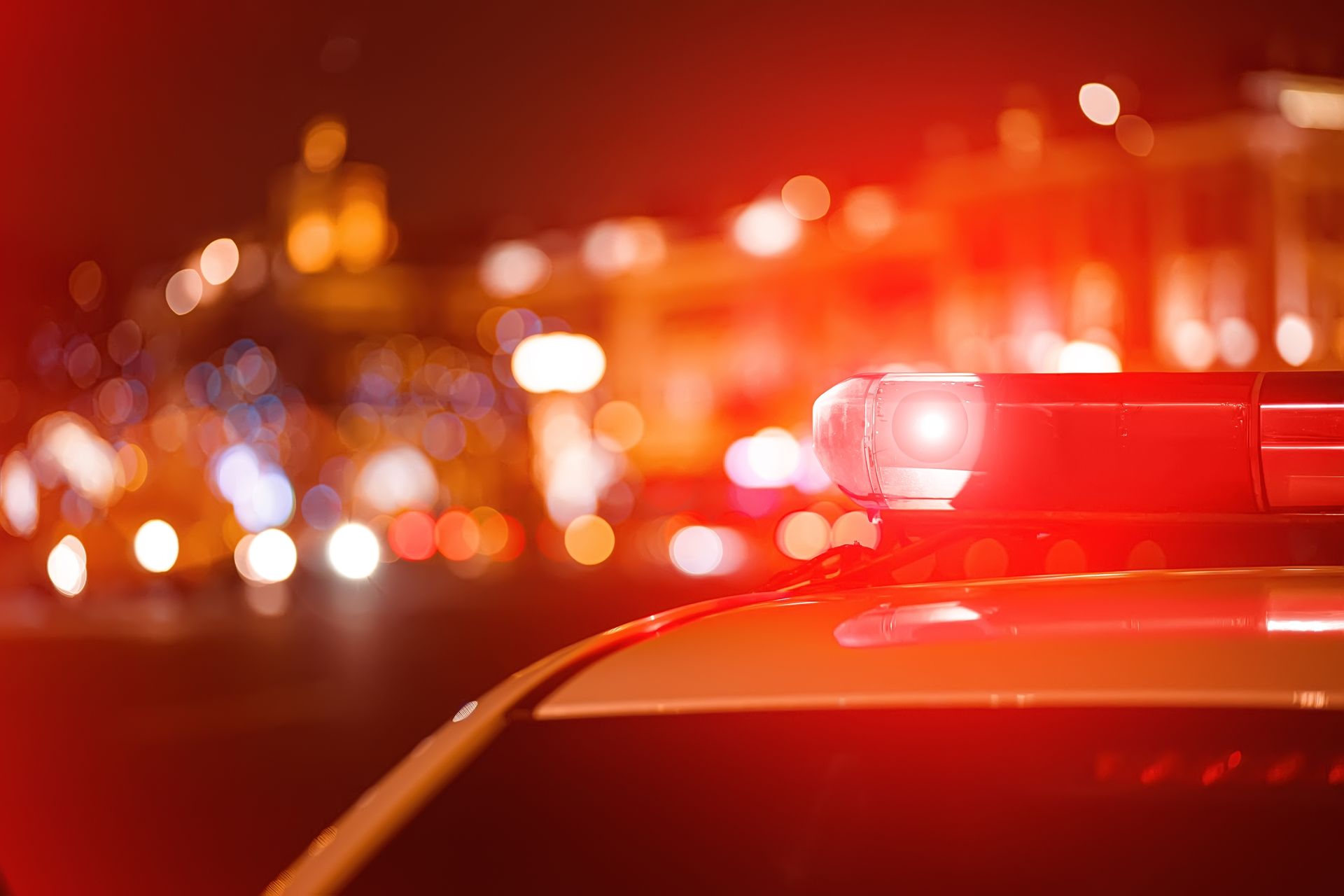 A bright red police emergency light mounted on top of a car at night with a blurred city background.
