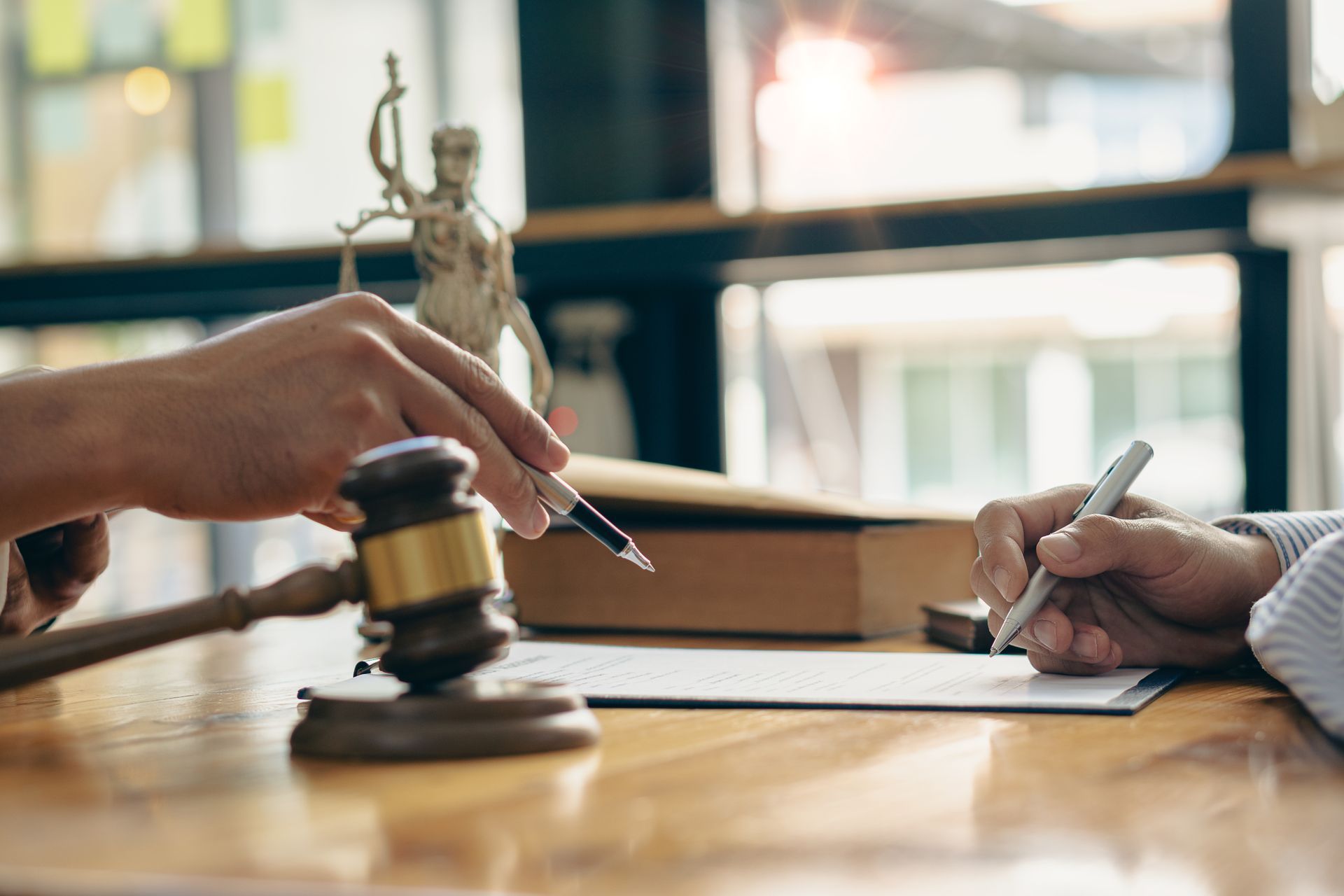 A lawyer and client review a legal document on a wooden desk featuring a gavel and a statue of Lady Justice.