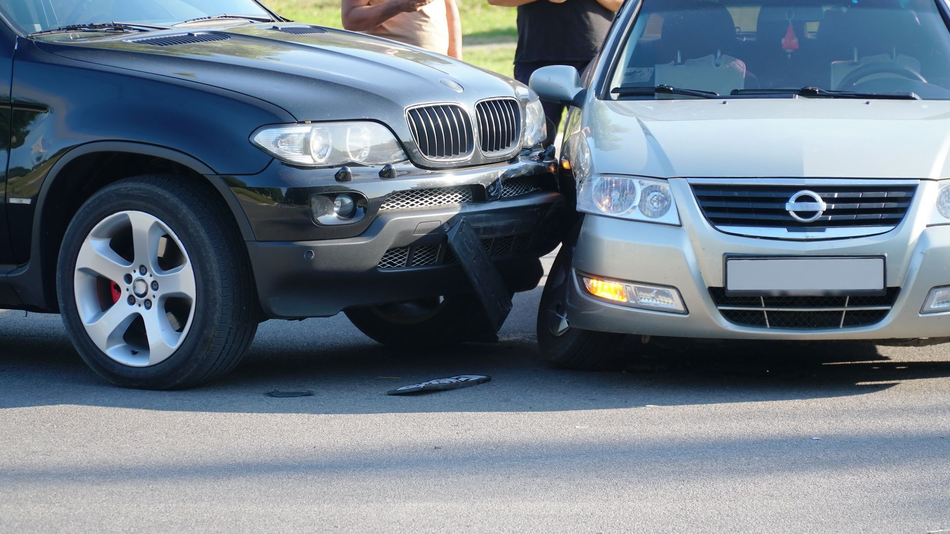 A black SUV and a silver Nissan car collided on an asphalt road.