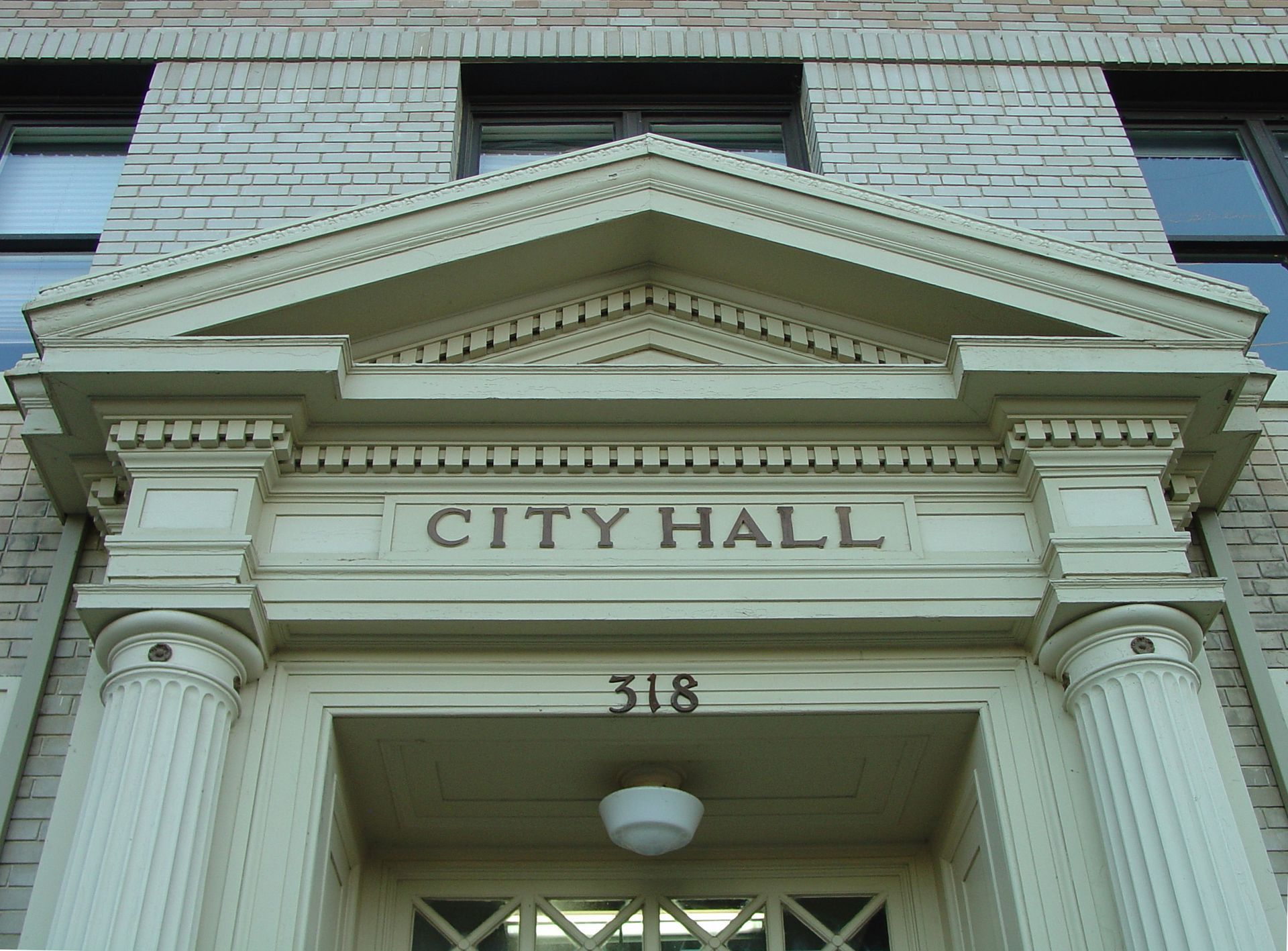 The entrance to a brick City Hall building featuring a pediment, classical columns, and the number 318 above the door.