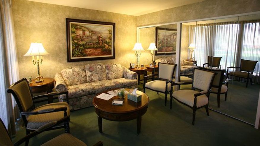 Cozy hotel lounge with floral sofa, armchairs, coffee table, lamps, and a scenic wall painting