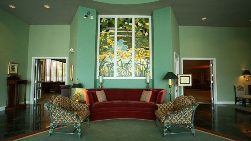 Elegant living room with green walls, red sofa, patterned chairs, and large window framed by trees.