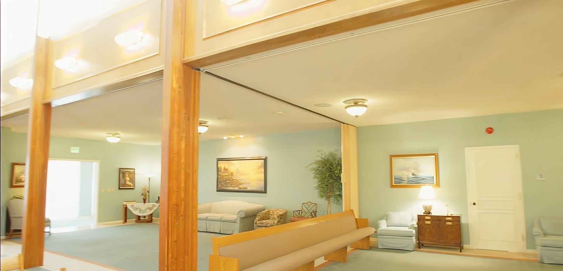 Bright hotel-style lobby with beige seating, wood accents, wall art, and a desk beside a white door