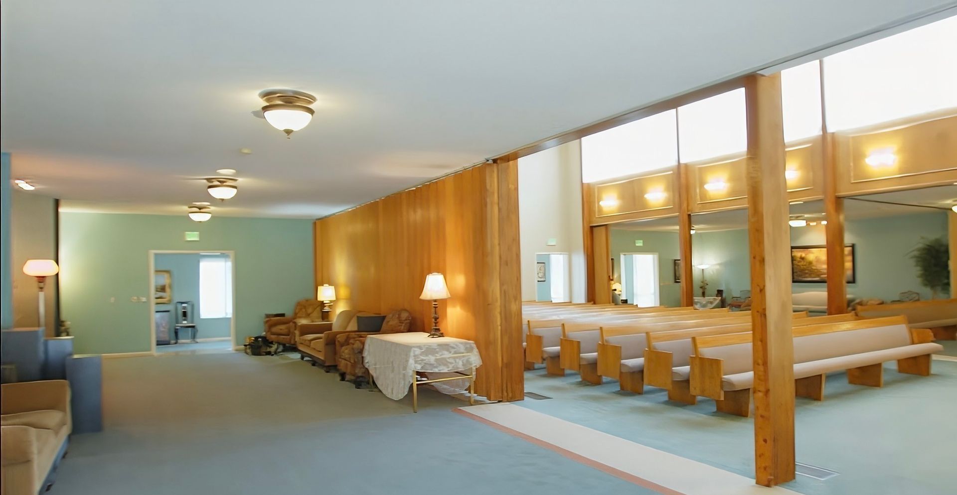Spacious public restroom with wooden stalls, long mirror-lit counters, and blue carpeted floor