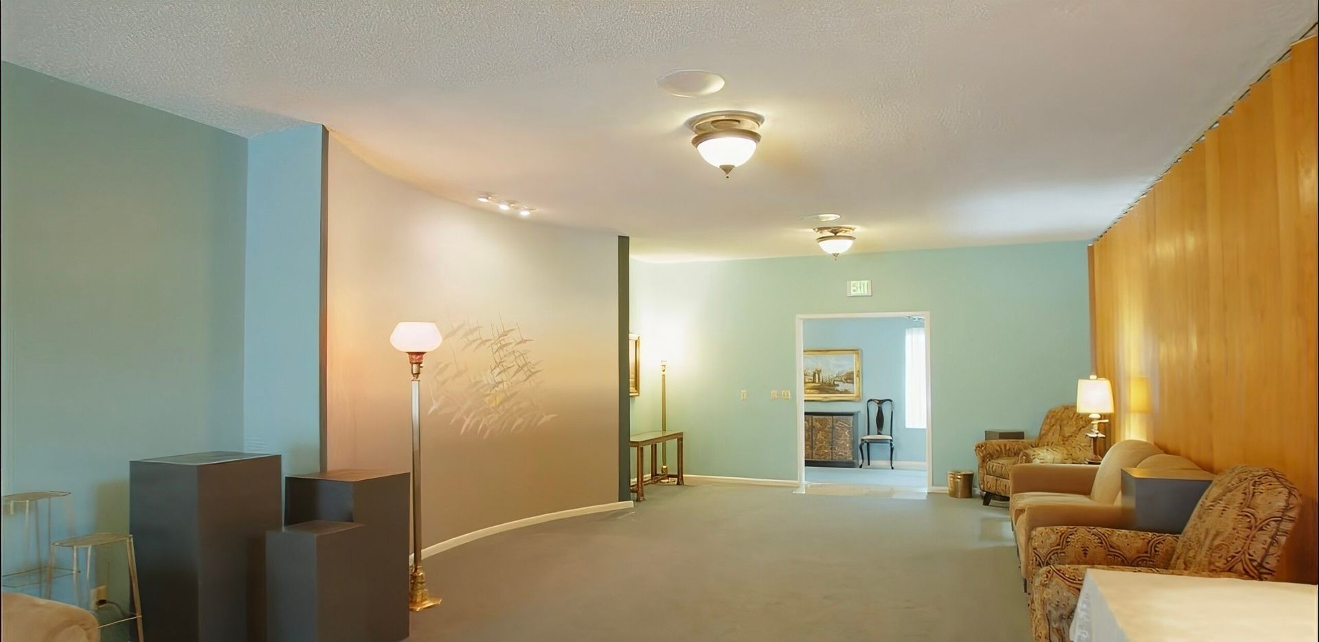 Spacious living room with blue walls, beige carpet, wooden accent wall, and sofas under a ceiling light.
