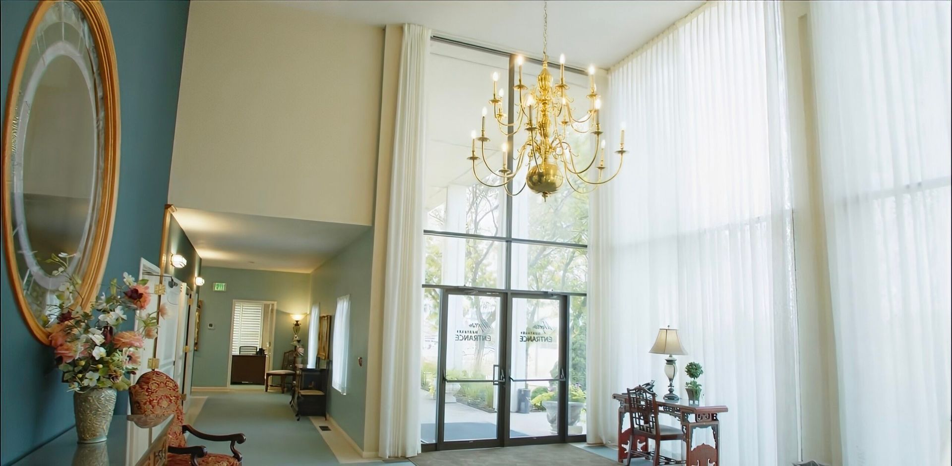 Elegant hotel lobby with tall windows, chandelier, and ornate mirror in soft blue and cream tones