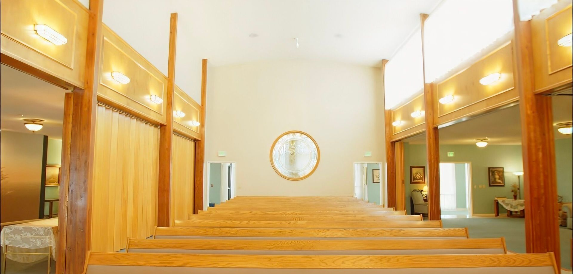 Wood-paneled interior with long pews, mirrored walls, and a clock centered on the far wall.