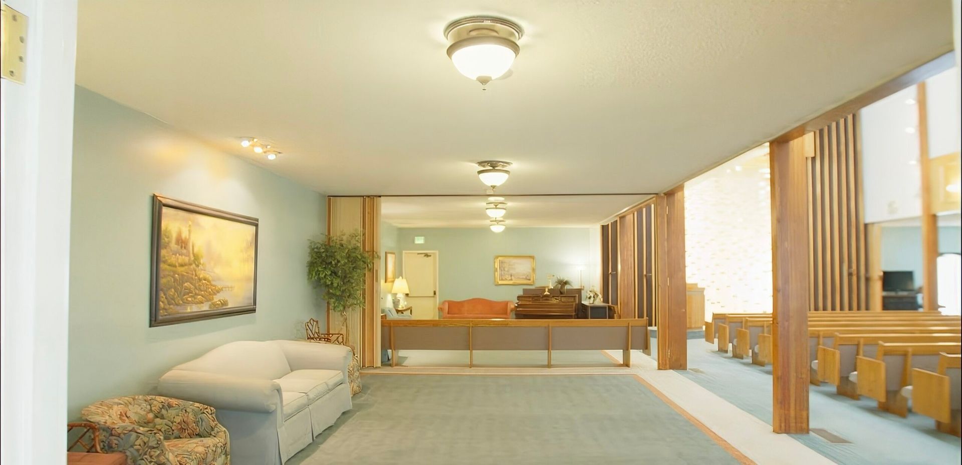 Bright hotel room with two beds, beige carpet, wooden furniture, and large windows.