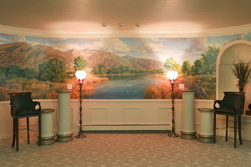 Lobby mural with mountain landscape, two lit floor lamps, and chairs on either side
