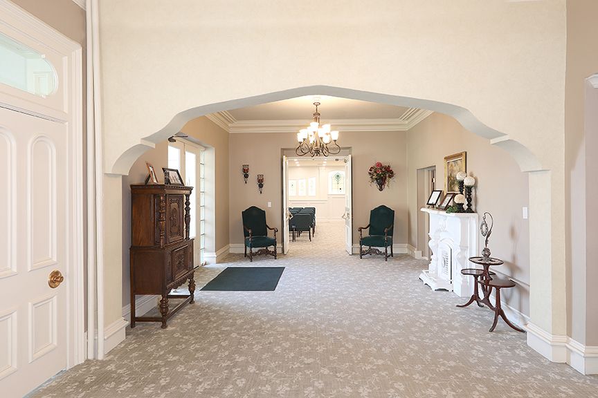 Elegant hallway with arched doorway, chandelier, chairs, and decorative furniture on carpeted floor.