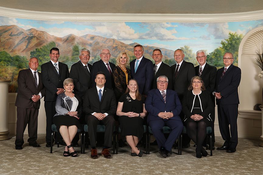 Group portrait of twelve people in formal attire standing and seated before a painted landscape backdrop
