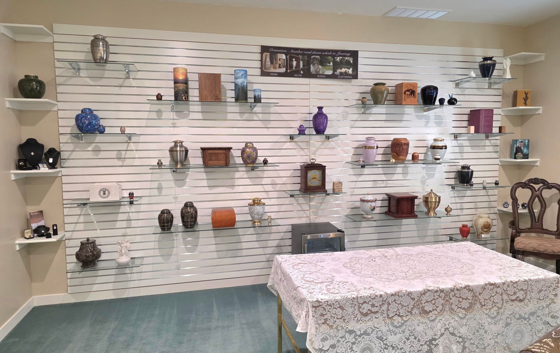 Display room with wall-mounted shelves of decorative pottery and a floral-covered table in the foreground