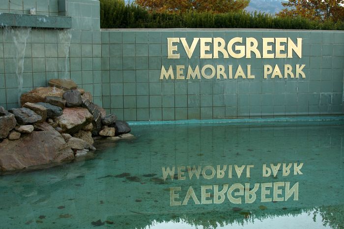 Evergreen Memorial Park sign reflected in a green-tinted water pool beside rocks and tiled wall