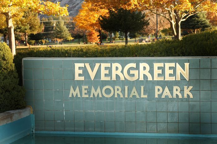 Evergreen Memorial Park sign on a green wall with autumn trees in the background