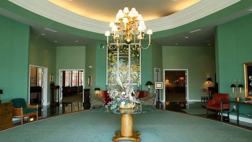 Elegant green lobby with a chandelier, floral centerpiece, and teal carpeting