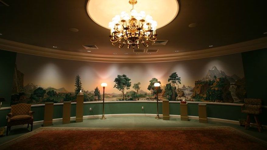 Elegant banquet hall with green chairs, round tables, and a large chandelier under warm lighting