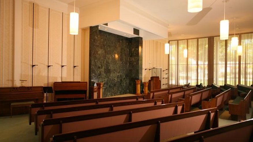 Empty church interior with wooden pews, hanging lights, and an altar at the front