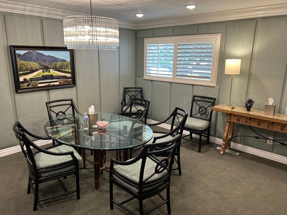 Modern waiting room with round glass table, black chairs, sideboard, lamp, and framed landscape art.