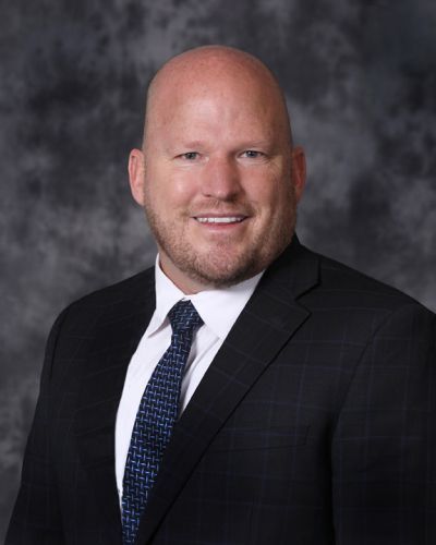 Smiling bald man in a dark suit and tie against a gray studio backdrop