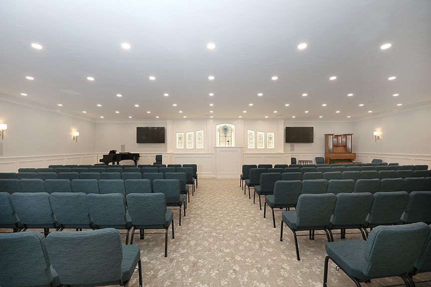 Bright church sanctuary with rows of blue chairs facing a lectern and piano under recessed lights