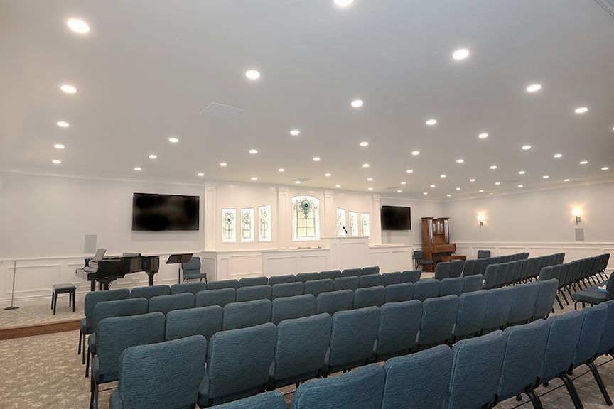 Bright church sanctuary with rows of blue chairs, white walls, and recessed ceiling lights