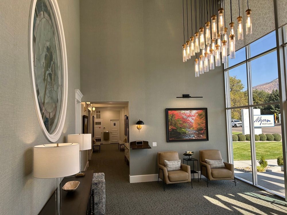 Modern lobby with tall windows, pendant lights, framed art, and seating chairs by a bright entrance.