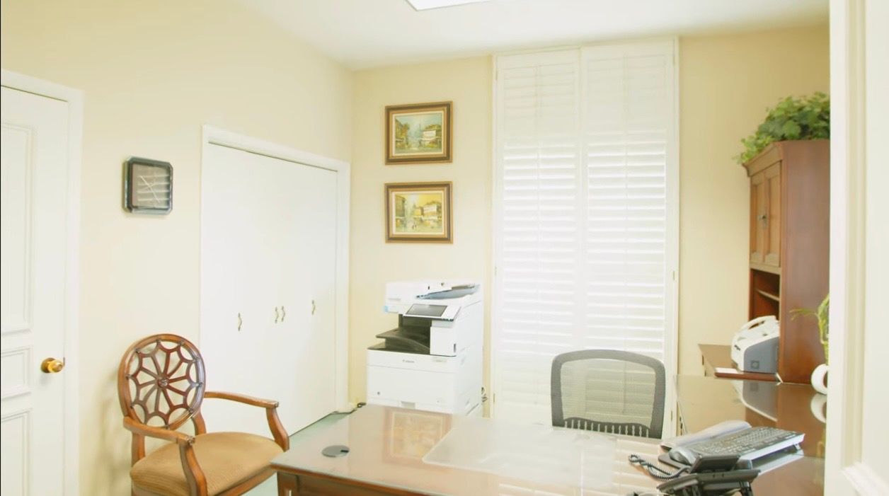 Bright home office with desk, printer, wooden chair, white walls, and a window with blinds