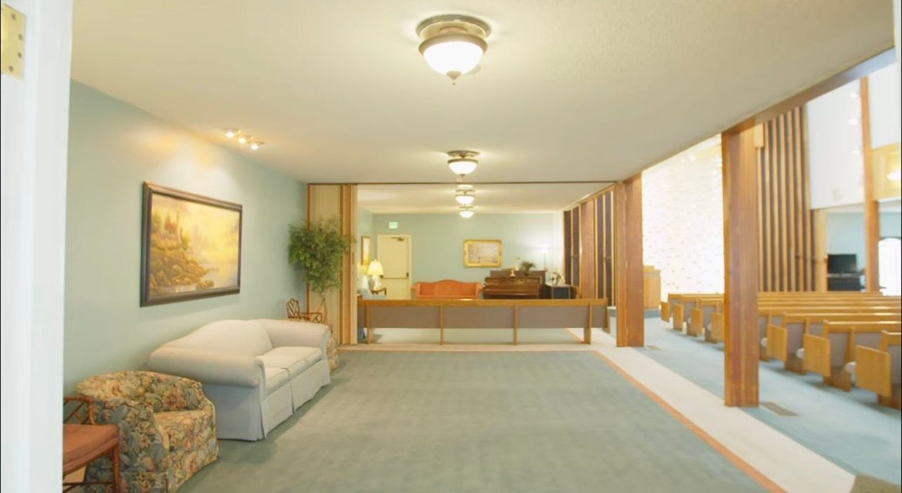 Bright, empty living room with a couch, armchair, desk, and large windows along the right wall.