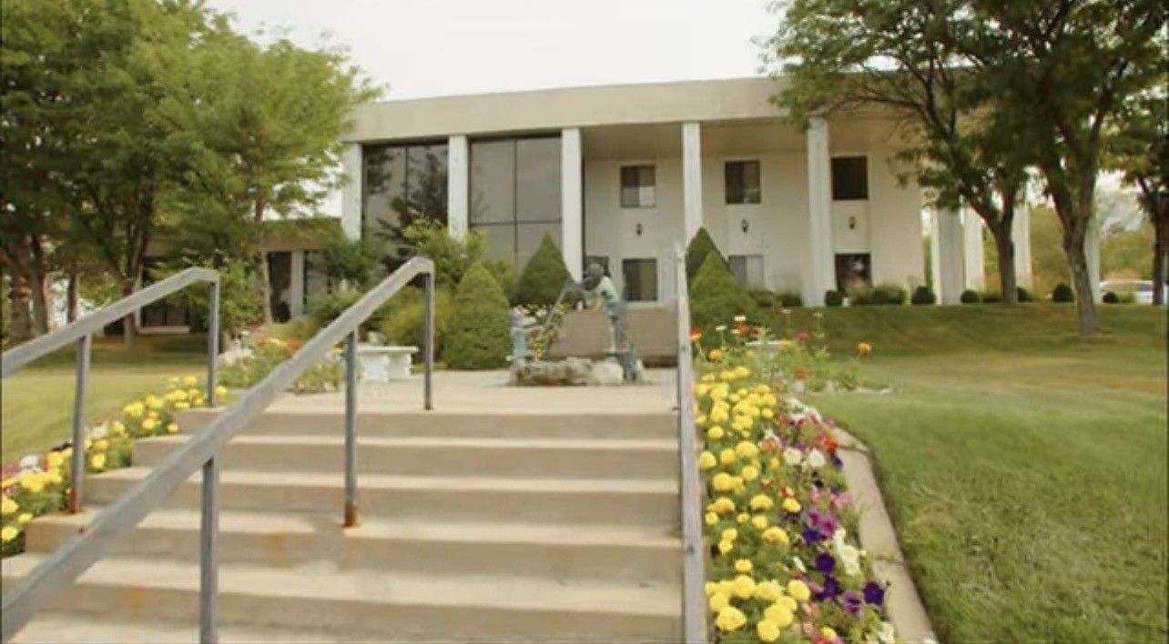 Front steps leading to a white building with columns, framed by flower beds and trees