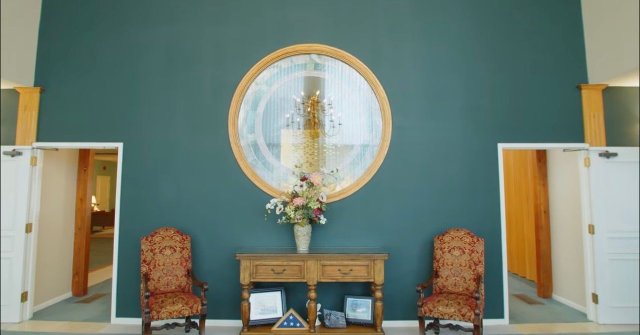 Elegant lobby with teal wall, round mirror, console table with flowers, and two upholstered chairs.