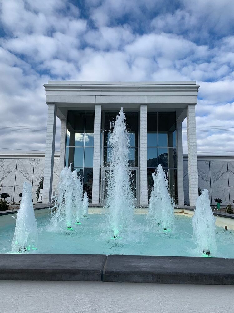 Modern fountain with water jets in front of a white building under a cloudy sky
