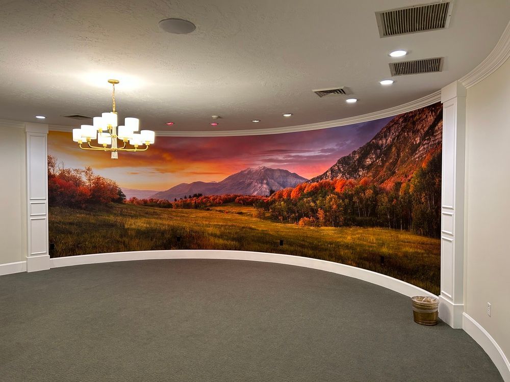 Curved empty room with a large mountain sunset mural, gray carpet, and a chandelier ceiling light.