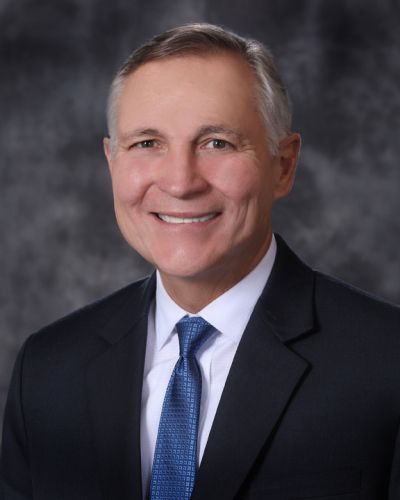 Smiling man in a dark suit and blue tie against a gray studio background