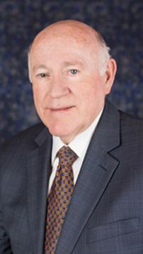 Studio portrait of a man in a dark suit and patterned tie against a blue background