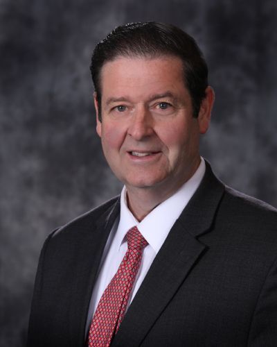 Formal portrait of a man in a dark suit and red tie against a gray studio backdrop