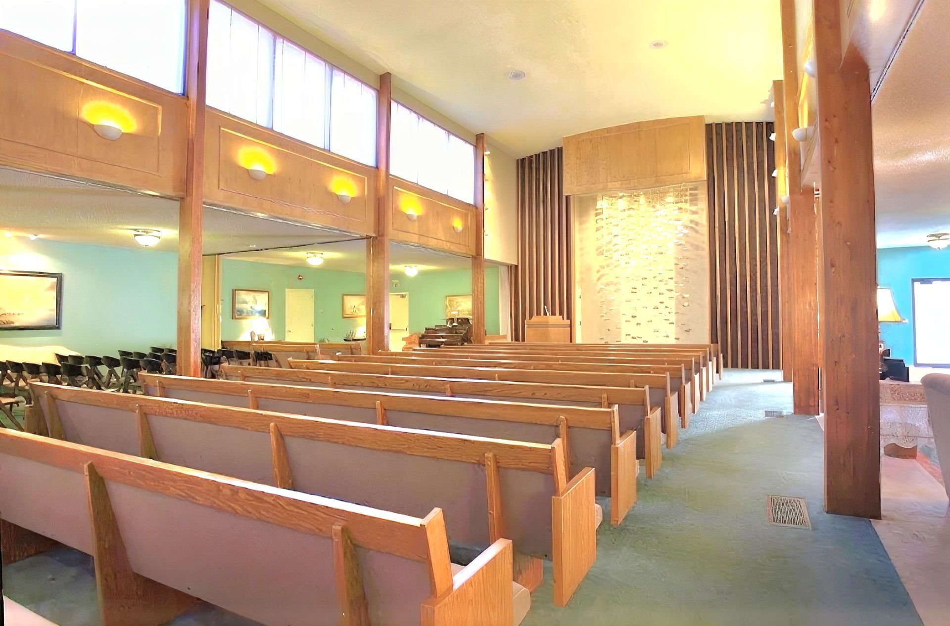Empty church sanctuary with wooden pews, tall pillars, and warm yellow lighting
